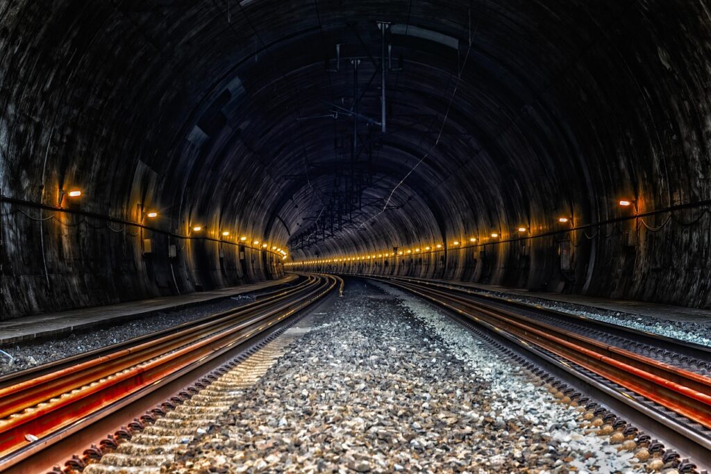 Tågspår i en tunnel med belysning längs väggarna.