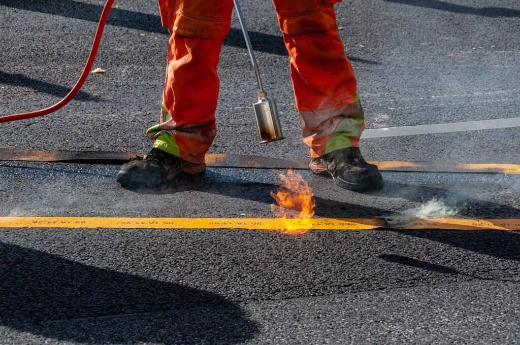 En vägbanepersonal i orange arbetskläder arbetar med asfalt på en väg.