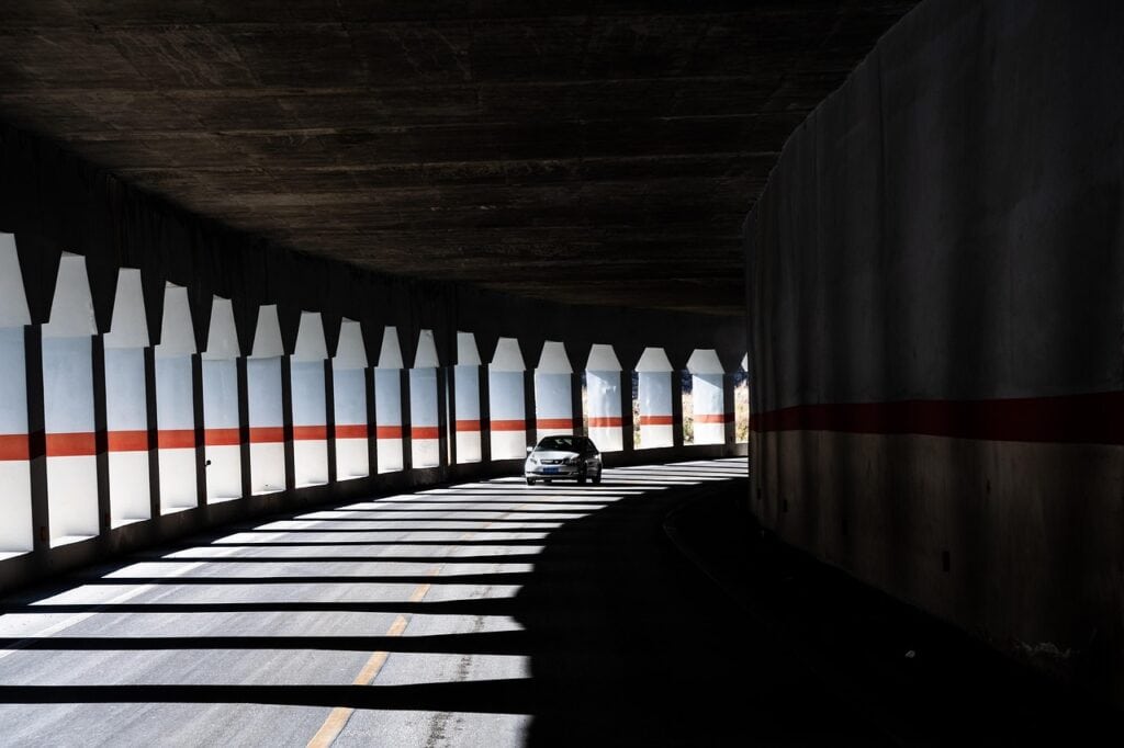 En bil kör genom en mörk vägtunnel med ljusinsläpp från sidorna.