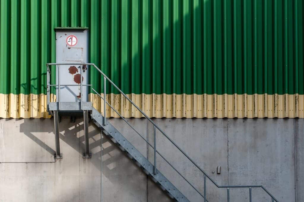 Grön och grå industribyggnad med utvändig trappa och dörr.