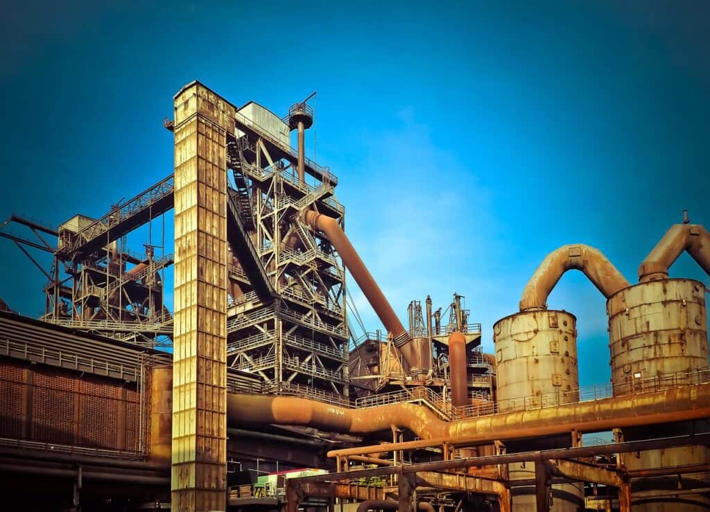 En stor industriell stålverksanläggning med masugn, rör och metallkonstruktioner mot blå himmel.