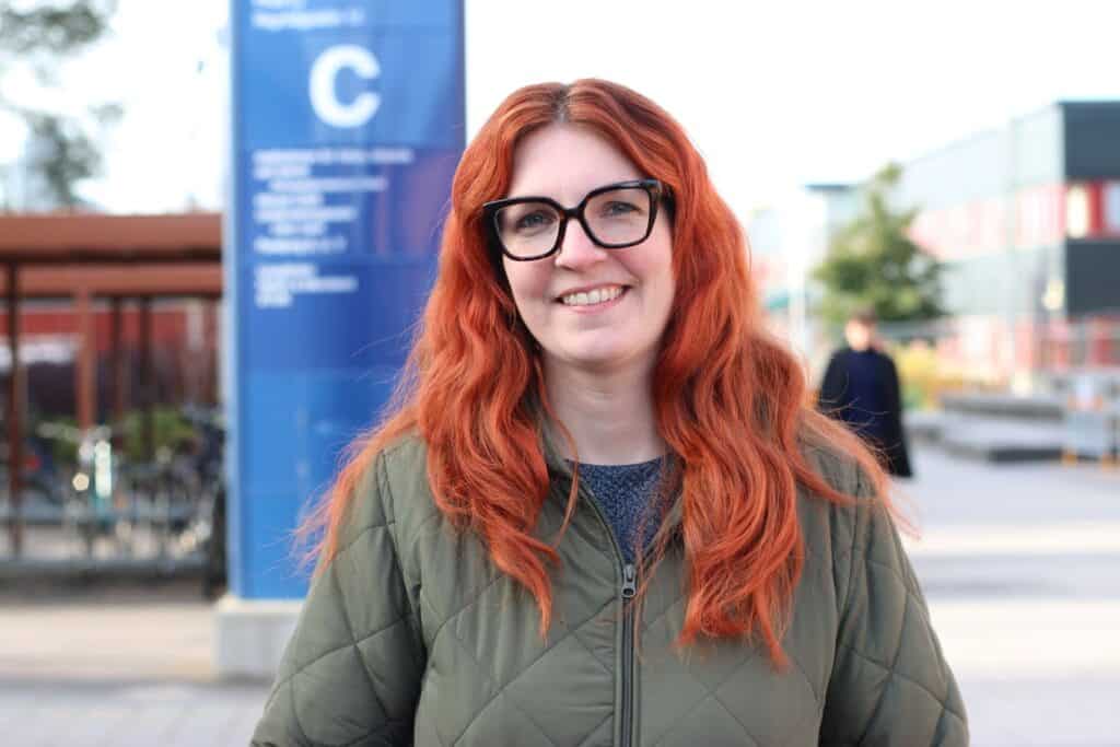 Ida Edskär står utomhus framför en blå skylt och ler mot kameran.