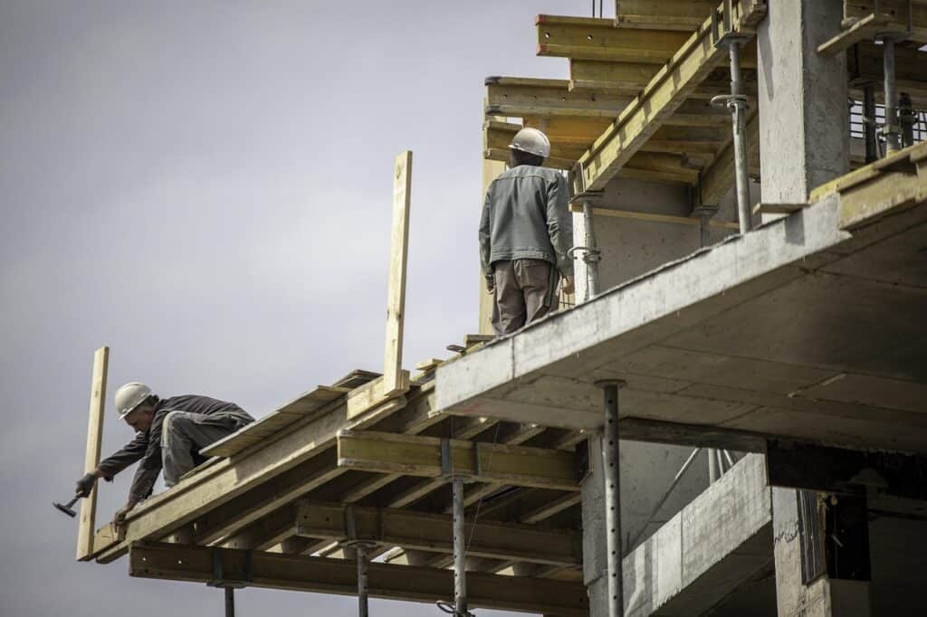 Två byggarbetare på en byggarbetsplats med träform och betongkonstruktion.