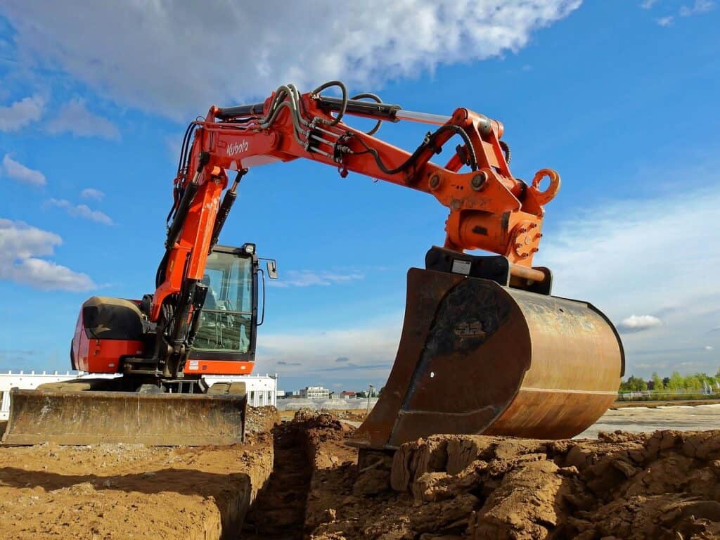 Orange grävmaskin av märket Kubota som schaktar i en grop på en byggarbetsplats under blå himmel med moln.