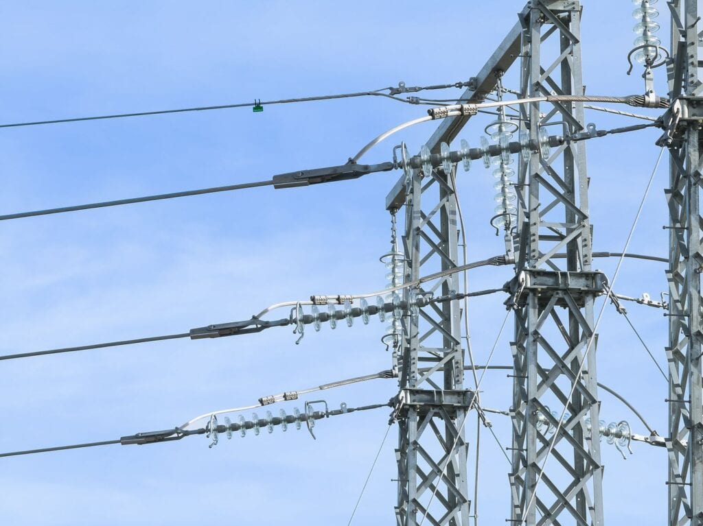 Högspänningsstolpar av metall med isolatorer och linor mot blå himmel.
