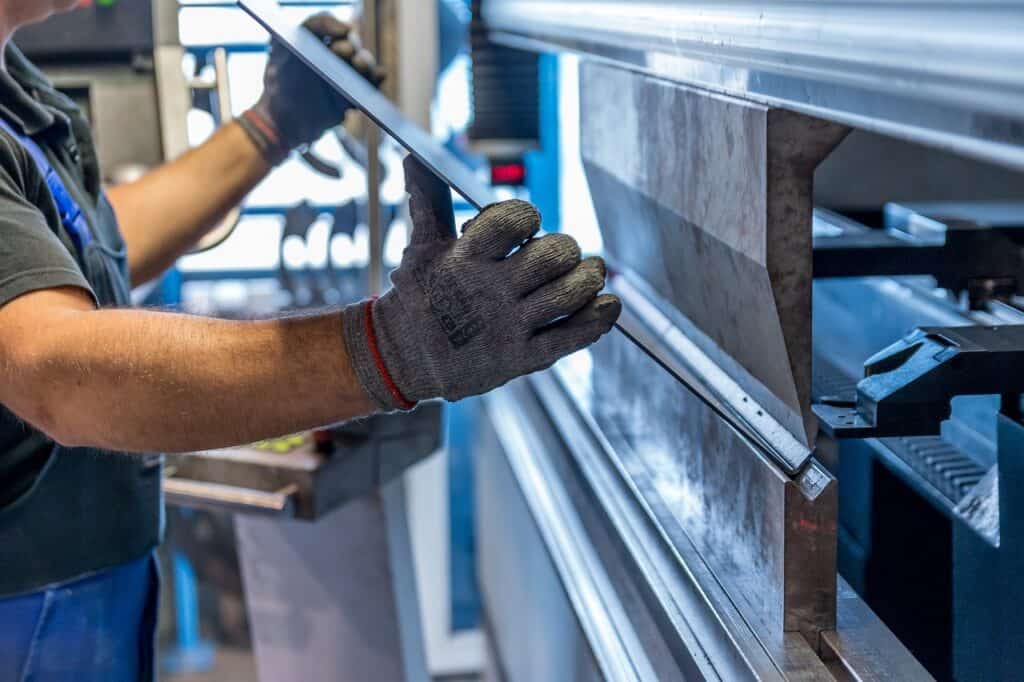 En person med arbetshandske håller en metallplåt i en plåtbockningsmaskin i en verkstad.