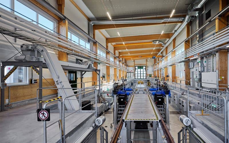 Interiör med en lång svarvanläggning i en verkstadshall med trästomme och blå maskiner längs spåren.