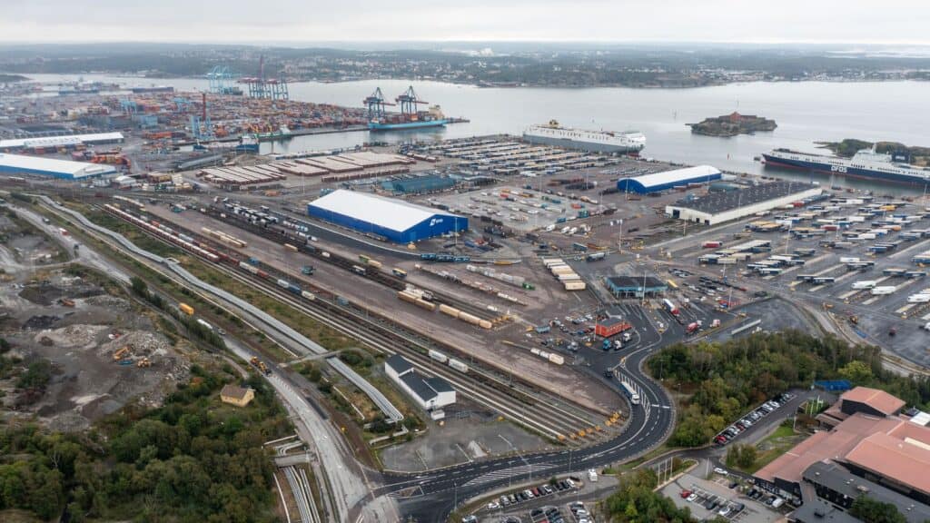 Flygfoto över Arken Kombiterminal med järnvägsspår, uppställda containrar och trailers, hamnkranar och fartyg i bakgrunden.
